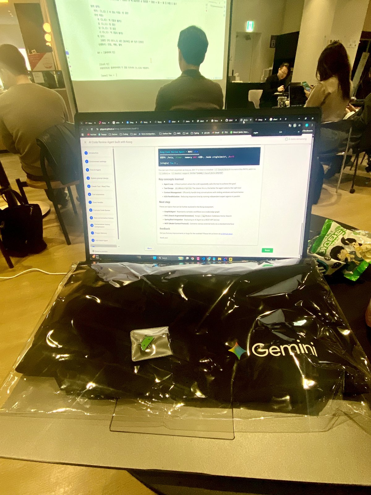 노트북에 열린 Koog 코드랩, 그 아래 놓인 Gemini 토트백과 안드로이드 핀